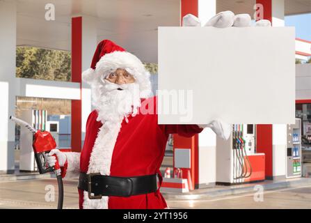 Der Weihnachtsmann hält eine Kraftstoffspritzpistole und eine leere Karte an einer Tankstelle Stockfoto