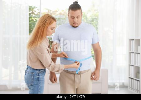 Ernährungswissenschaftler, der die Taille eines übergewichtigen Mannes mit Klebeband in der Klinik misst Stockfoto