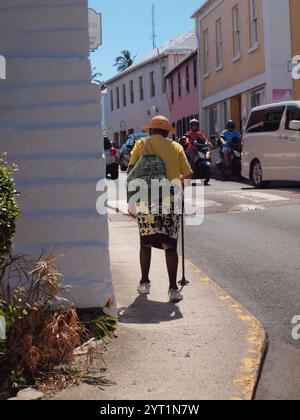 Ältere Bermuda-Bewohner, die mit einem Stock in St. Georges laufen. Ein schmaler Bürgersteig zu überqueren ist schwierig. Stockfoto