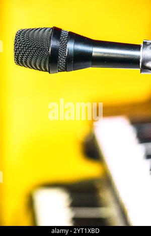 Ein Mikrofon steht gut sichtbar im Vordergrund und ist einsatzbereit. Im Hintergrund verleiht eine Tastatur der lebhaften Atmosphäre der s eine musikalische Note Stockfoto