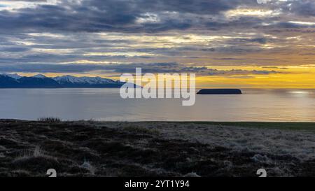 Skjalfandi (Skjalfandafloi) Fjord in Nordisland, Blick auf den orangefarbenen Sonnenuntergang mit schneebedeckten Viknafjoll- und Kinnarfjoll-Gebirgszügen, dramatischer Himmel. Stockfoto