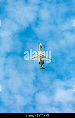 Ein Flugzeug fliegt am Himmel über einem blauen und bewölkten Himmel. Das Flugzeug ist ein kleiner Jet mit einem roten und weißen Schwanz. Der Himmel ist klar und blau, mit ein paar cl Stockfoto