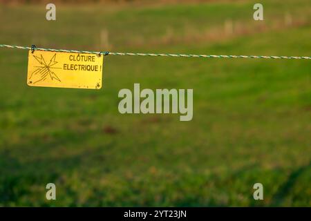 Elektrische Zaunplatte in der französischen Landschaft. Das Schild warnt die Besucher vor den Gefahren des elektrischen Zauns. Stockfoto