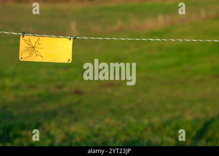 Elektrische Zaunplatte in der französischen Landschaft. Das Schild warnt die Besucher vor den Gefahren des elektrischen Zauns. Stockfoto