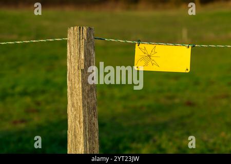 Elektrische Zaunplatte in der französischen Landschaft. Das Schild warnt die Besucher vor den Gefahren des elektrischen Zauns. Sicherheitszaun mit Hochspannung si Stockfoto