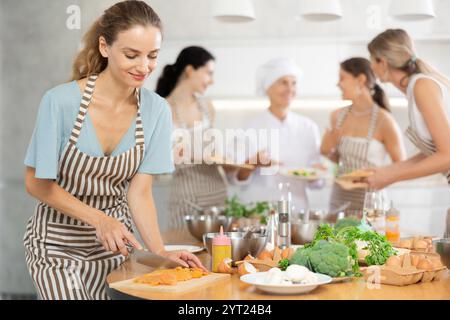 Mädchen in der Kochschule schneidet Hühnchen und bereitet kalorienarmes Mittagessen zu Stockfoto