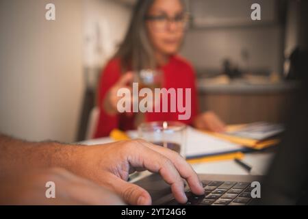 Ein Mann tippt auf einem Laptop, während eine Frau in einem roten Pullover neben ihm sitzt Stockfoto