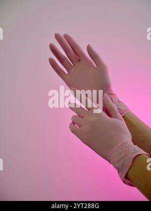 Weibliche Kosmetologin Krankenschwester mit rosa Nahaufnahme medizinischen Handschuhen auf weißem Hintergrund, vertikal, Zeitlupe Stockfoto