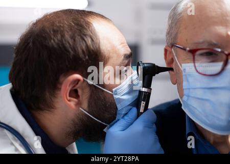 Männlicher Rentner wird einer detaillierten Ohruntersuchung unterzogen, da ein erfahrener hno-Spezialist während des klinischen Termins ein Otoskop besitzt. Nahaufnahme des jungen Arztes mit sorgfältiger Anwendung des otologischen Werkzeugs beim älteren Mann im Krankenhaus. Stockfoto