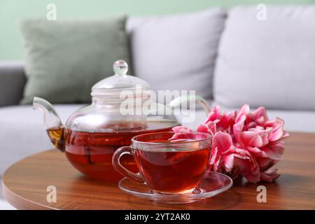 Transparente Tasse Tee und Teekanne auf dem Tisch mit Tulpenblüten im Wohnzimmer Stockfoto