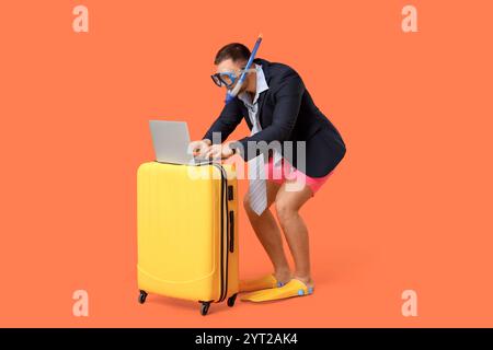 Junge Büroangestellte in Tauchmaske mit Laptop und Koffer auf orangem Hintergrund Stockfoto