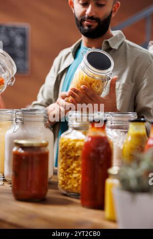 Männlicher Kunde bewundert ein Glasgefäß, das in einem Lebensmittelgeschäft mit einem Bio-Produkt gefüllt ist. Nahaufnahme eines Mannes aus dem Nahen Osten, der frische organische Gegenstände in einem plastikfreien Behälter untersucht. Stockfoto