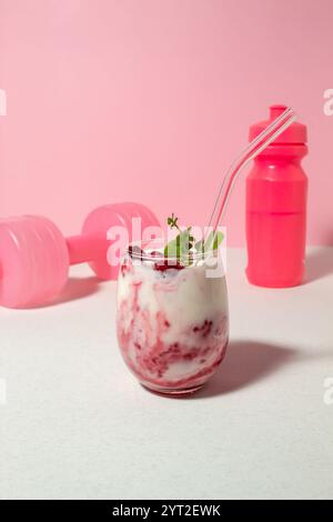 Obstjoghurt mit Himbeeren und Mentha im Glas, rosa Hantel und eine Flasche Wasser. Das Konzept des gesunden Lebens Stockfoto