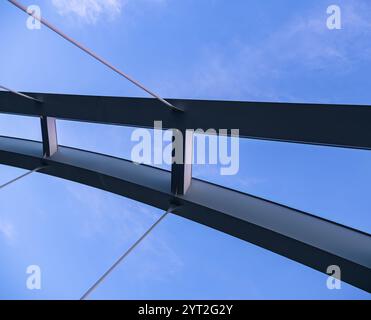 Stockholm, Schweden - 24. Mai 2024: Eine schlanke, moderne Brücke mit gebogenen Balken und Kabeln erstreckt sich vor einem hellblauen Himmel. Stockfoto