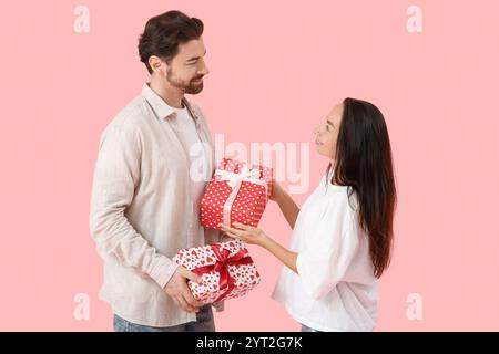 Liebevolles Paar, das Geschenke auf rosa Hintergrund austauscht. Valentinstag-Feier Stockfoto
