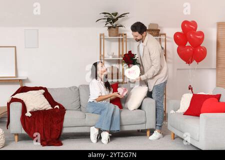 Liebevolles Paar, das zu Hause Geschenke und Blumen austauscht. Valentinstag-Feier Stockfoto