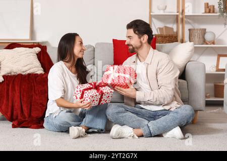 Liebevolles Paar tauscht zu Hause Geschenke auf Teppich aus. Valentinstag-Feier Stockfoto
