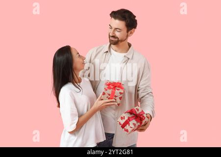 Liebevolles Paar, das Geschenke auf rosa Hintergrund austauscht. Valentinstag-Feier Stockfoto