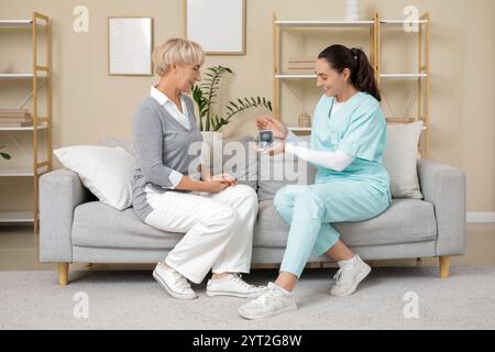Arzt gibt reiferen Frauen Hörhilfe, während sie zu Hause besuchen Stockfoto