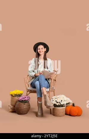 Stilvolle junge Frau mit Chrysanthemen Blumen, die Buch im Sessel auf braunem Hintergrund lesen Stockfoto