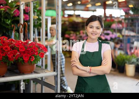 Verkäuferin im asiatischen Blumenladen steht neben einem Blumenständer mit Petunien Stockfoto