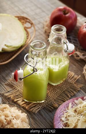 Zwei Flaschen Grünkohl- und Gurkensaft mit frischen roten Äpfeln auf einem Tisch Stockfoto