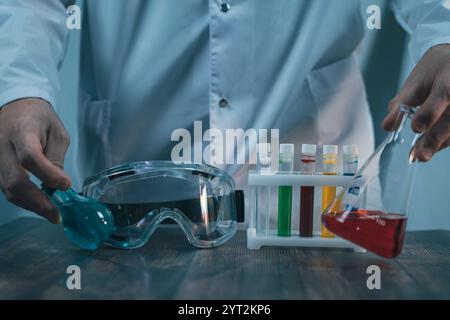 Ein Laboraufbau mit bunten Reagenzgläsern, Schutzbrillen und Kolben mit blauen und roten Flüssigkeiten auf einer Holzoberfläche. Chemieexperiment und r Stockfoto
