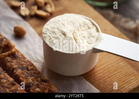 Eine Schaufel Molkenproteinpulver mit hausgemachten, gesunden No-Bake-Bars und Erdnüssen im Hintergrund Stockfoto