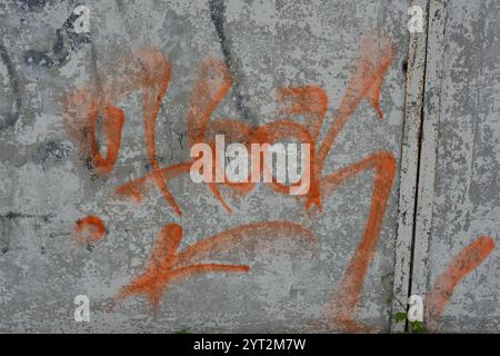 Zeichnungen, Graffiti, Inschriften auf einem alten Stahlbetonzaun, Ziegelmauern. Ungewöhnlicher Text, orangefarbene Signatur mit Sprühfarbe. Stockfoto