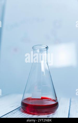 Erlenmeyerkolben aus Glas mit roter Flüssigkeit auf weißer Oberfläche. Wissenschaftliches Experiment, Chemie, Forschung, Laborausrüstung, sterile Umgebung Stockfoto