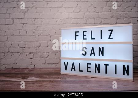 Leuchtkasten mit „Happy Valentine's Day“-Text auf Holztisch und Backsteinwand Stockfoto