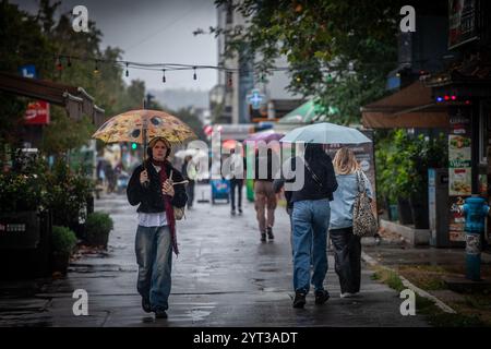 NOVI SAD, SERBIEN - 12. SEPTEMBER 2024: Menschen, die mit Regenschirmen auf Bulevar Oslobodjenja in Novi Sad an einem regnerischen Nachmittag spazieren gehen. Bulevar oslobodjenj Stockfoto