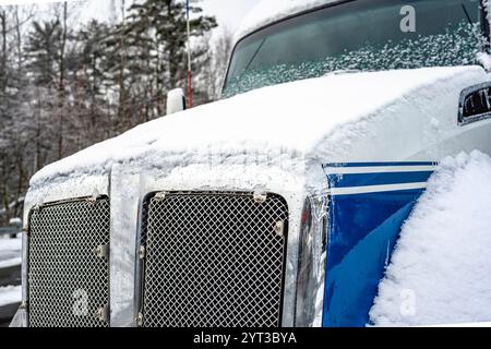 Frontteil der leistungsstarken Motorhaube in Industrieausführung, weiß und blau, Big Rig, mit verchromtem Kühlergrill, der mit Schnee und Eis bedeckt ist, steht auf dem truc Stockfoto