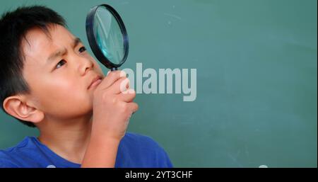 Vorderansicht des asiatischen Schuljungen, der durch Lupe im Klassenzimmer in der Schule schaut Stockfoto