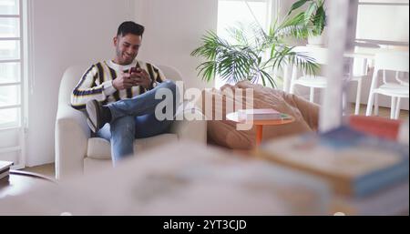Vorderansicht eines glücklichen birassischen Mannes, der in einem kreativen Büro arbeitet, mit dem Smartphone spricht und lächelt Stockfoto