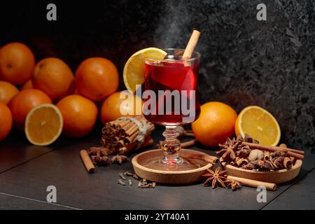 Glühwein mit Zutaten und frischen Orangen auf einem schwarzen Küchentisch. Stockfoto