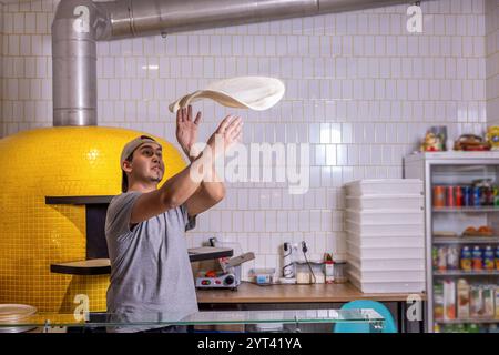 Der Koch wirft Pizzateig. Der Pizzakoch lässt den Pizzateig in der Luft drehen, um ihn dünn und weich zu machen. Pizzabäcker, der Teig in der Küche spinnt Stockfoto