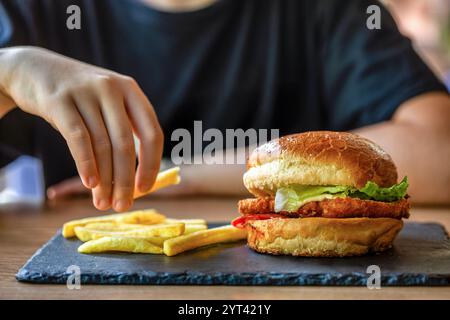 Der Mann hält den Burger in der Hand. Mahlzeit mit Burger und Pommes frites. Hamburger. Cheeseburger, handgeschnittene Pommes frites. Handburger, Nahaufnahme. Frau in der Hand Stockfoto