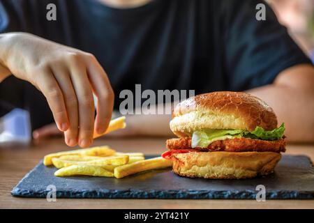 Der Mann hält den Burger in der Hand. Mahlzeit mit Burger und Pommes frites. Hamburger. Cheeseburger, handgeschnittene Pommes frites. Handburger, Nahaufnahme. Frau mit Delic Stockfoto