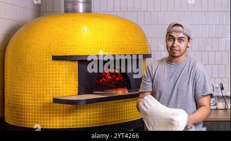 Der Pizzakoch arbeitet in der Küche. Koch bereitet Pizzateig zu. Der Prozess der Pizza. Ein erfahrener Koch bereitet Teig für Pizza zu, die mit Händen gerollt wird Stockfoto