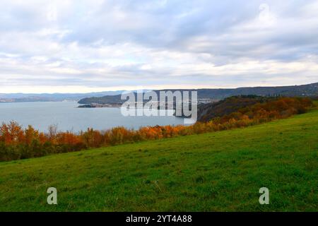 Blick auf eine grüne Wiese und herbstorange farbene Bäume an der Küste der Adria und Izola Stadt in Istrien, Küstenregion, Slowenien Stockfoto