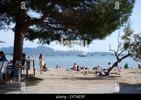 Der Strand von Port de Pollenca, vom Pine Walk aus gesehen, mit Leuten, die an Restauranttischen auf den vorgelagerten Mallorca Balearen Inseln saßen Stockfoto