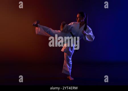 Junge Frau im Kimono, die Karate auf dunklem Hintergrund übt Stockfoto