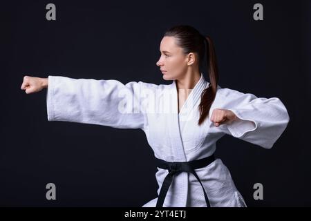 Junge Frau im Kimono, die Karate auf schwarzem Hintergrund übt Stockfoto