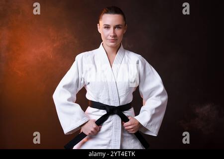 Junge Frau im Kimono, die Karate auf dunklem Hintergrund übt Stockfoto