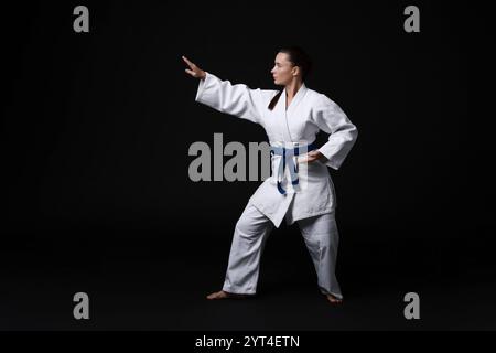 Junge Frau im Kimono, die Karate auf schwarzem Hintergrund übt Stockfoto