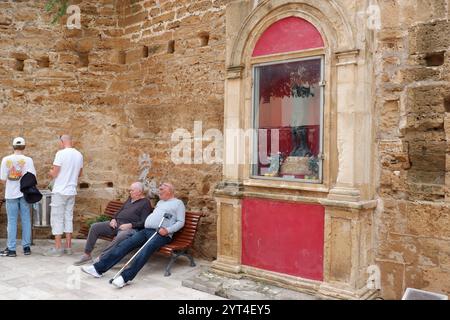 Mallorquinische Senioren, zwei ältere Männer unterhalten sich auf einer Bank neben einer Statue in einem Glaskasten in den Stadtmauern der Altstadt von Alcudia Mallorca Balearen Inseln Stockfoto