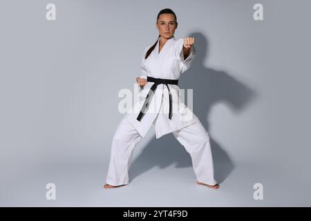 Junge Frau im Kimono, die Karate auf grauem Hintergrund übt Stockfoto