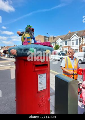 Postbote, der mit Trolley läuft und auf Postkiste blickt, mit Garn bombardiertem Topper portsmouth england uk Stockfoto