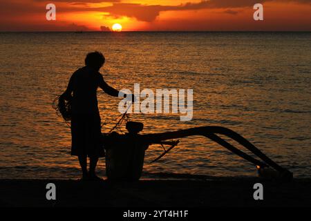 Silhouette eines Fischers und seines Bootes am Strand. Hintergrund des Sonnenuntergangs mit orangefarbenem Himmel Stockfoto